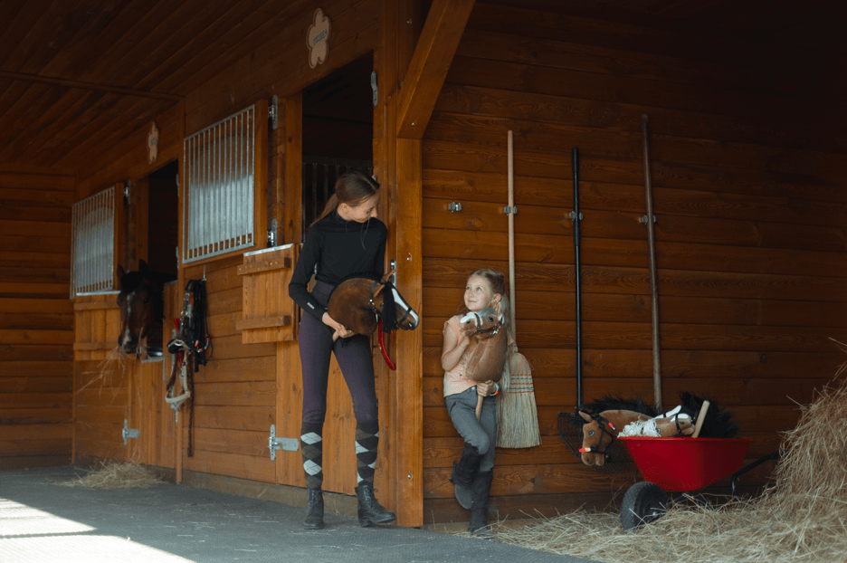 Jeunes avec des Hobby Horses devant les écuries en bois d’un club d’équitation