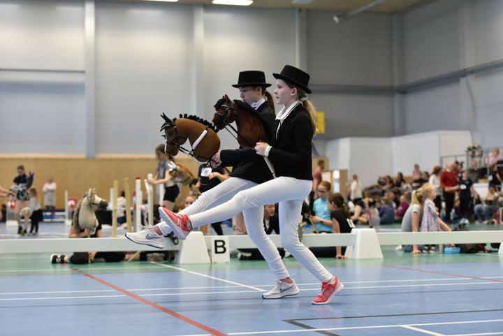 Deux enfants en tenues formelles de Hobby Horsing participant en intérieur avec des Hobby Horses