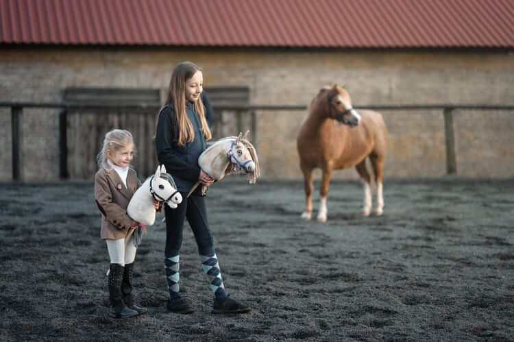 Deux enfants portant des Hobby Horses dans une carrière extérieure près d’un poney