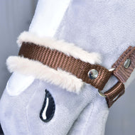 Gros plan sur la muserolle en sangle marron bordée de fourrure beige douce et son rivet argenté, sur un Hobby Horse gris en peluche