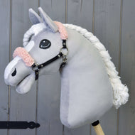 Een grijze pluche Hobby Horse met witte bles en gevlochten manen draagt de zwarte halster van kunstleer met oudroze bont