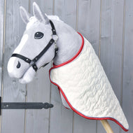 Grijze Hobby Horse met zwart halster in de crème gewatteerde reisdeken met rode rand over de hals