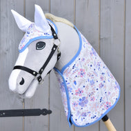 Hobby Horse gris clair avec licol noir portant la couverture fleurie et le bonnet d’oreilles assorti aux oreilles blanches, bordure bleue