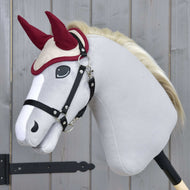 Hobby Horse gris clair à crinière blonde portant le bonnet d’oreilles Maroon Star et un licol noir devant une porte en bois grise