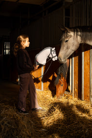 Meisje in donkere sweater in een stal houdt Hobby Horse Caesar in zwart hoofdstel bij een schimmel in zijn box