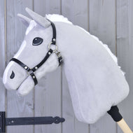 Hobby Horse gris en peluche à crinière blanche duveteuse et liste blanche, avec le licol en similicuir noir devant un mur en bois gris