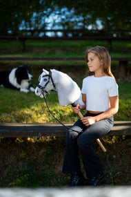Meisje in wit topje op een bank met de lichtgrijze Hobby Horse in een zwart hoofdstel, een bordercollie erachter