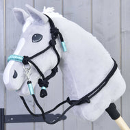 Hobby Horse gris portant le licol en corde noire à nœuds et enroulements turquoise, avec rênes noires assorties sur l’encolure