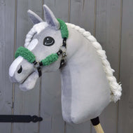 Grijze pluche Hobby Horse met gevlochten witte manen en de zwarte halster met groen bont voor een grijze houten wand