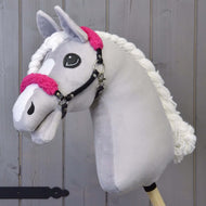 Een grijze pluche Hobby Horse met witte bles en gevlochten manen draagt de zwarte halster met krullend felroze bont