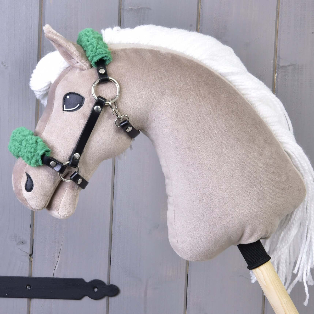 Hobby Horse beige à crinière blanche en fil portant le licol noir en similicuir avec fourrure verte sur la muserolle et la têtière