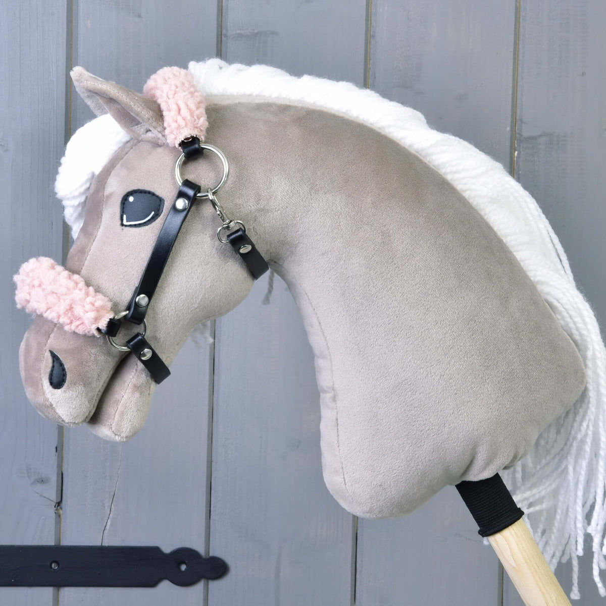 Een beige pluche Hobby Horse met witte manen draagt de zwarte halster met krullend oudroze bont op neusriem en kopstuk