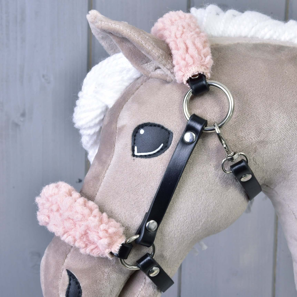 Close-up van de zwarte halster van kunstleer op een beige Hobby Horse, met krullend roze bont, zilveren ring en musketon