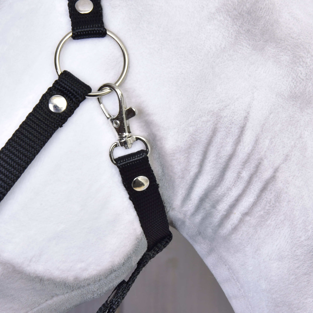 Gros plan sur l’anneau argenté et le mousqueton du licol noir contre la joue en peluche blanche du Hobby Horse Elektra