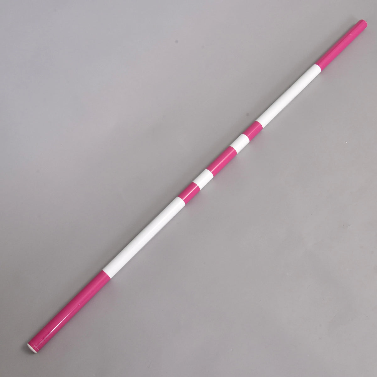 The pink and white striped pole of the jump lying diagonally on a light grey floor