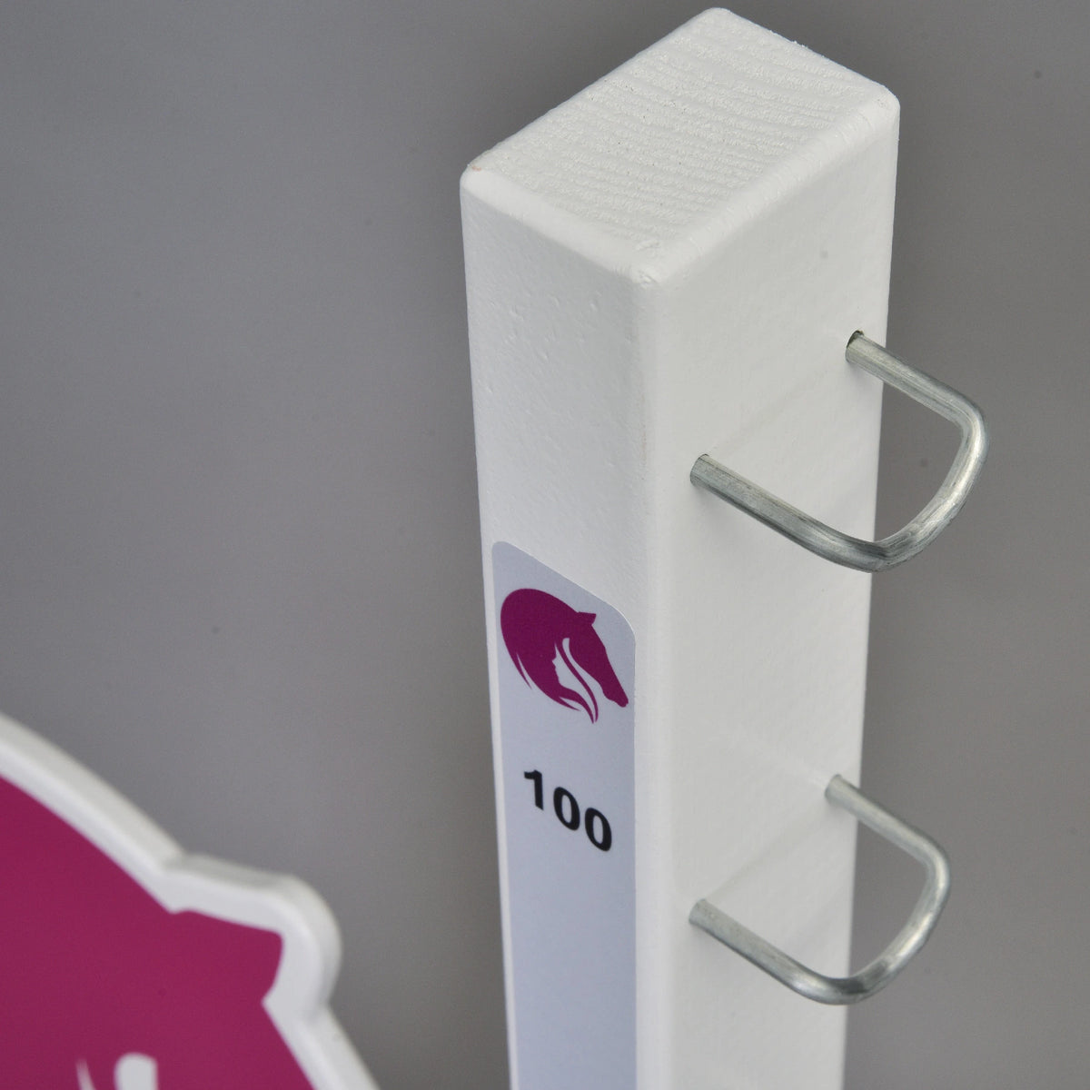 Close-up of the top of a white post with U-shaped metal hooks and a small pink horse logo above the 100 mark