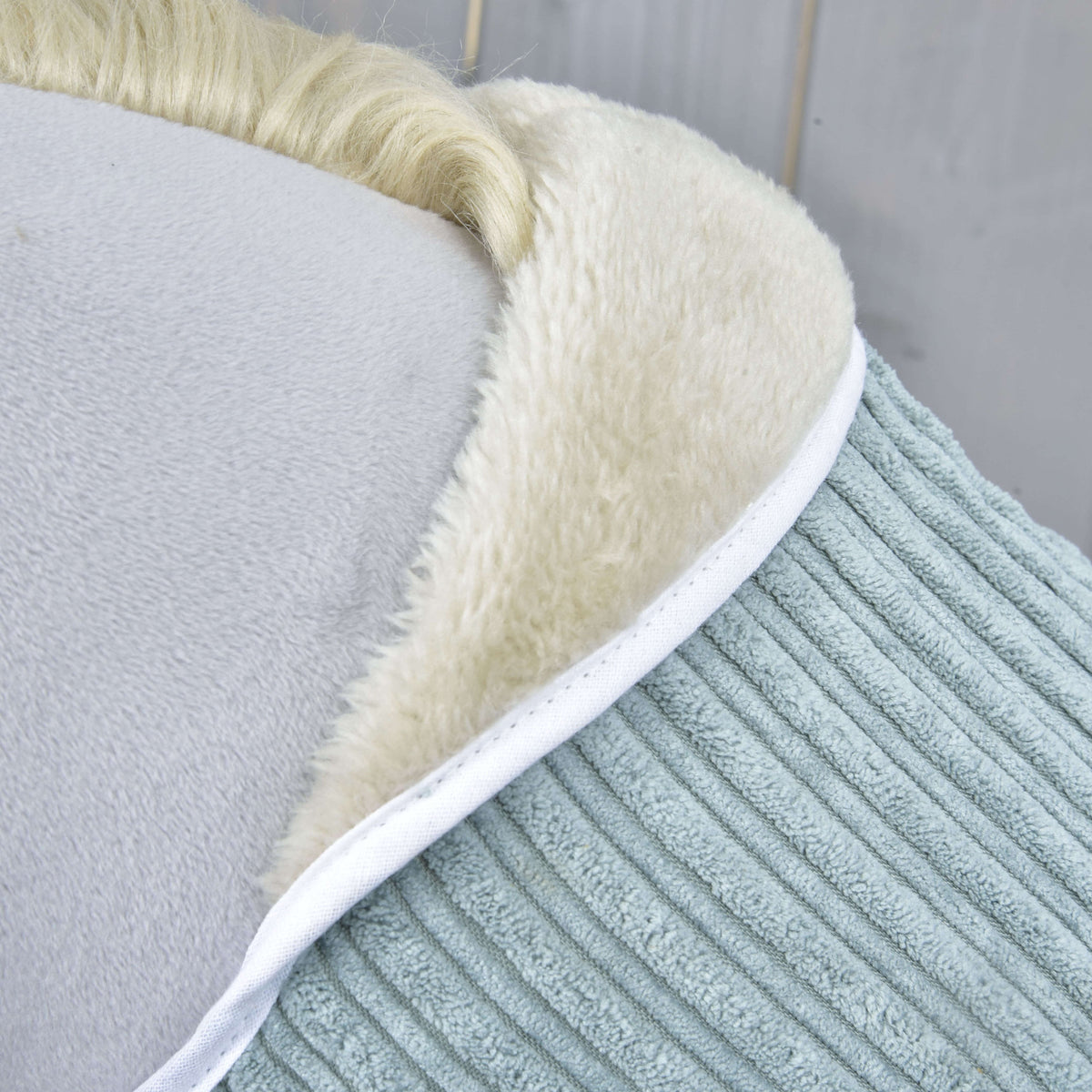 Détail du col en polaire crème bordé d’un passepoil blanc contre le large velours côtelé vert sauge de la couverture