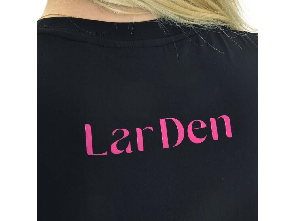 Gros plan de l’inscription rose LarDen au dos du T-shirt Active Hobby Horse noir, cheveux blonds au-dessus