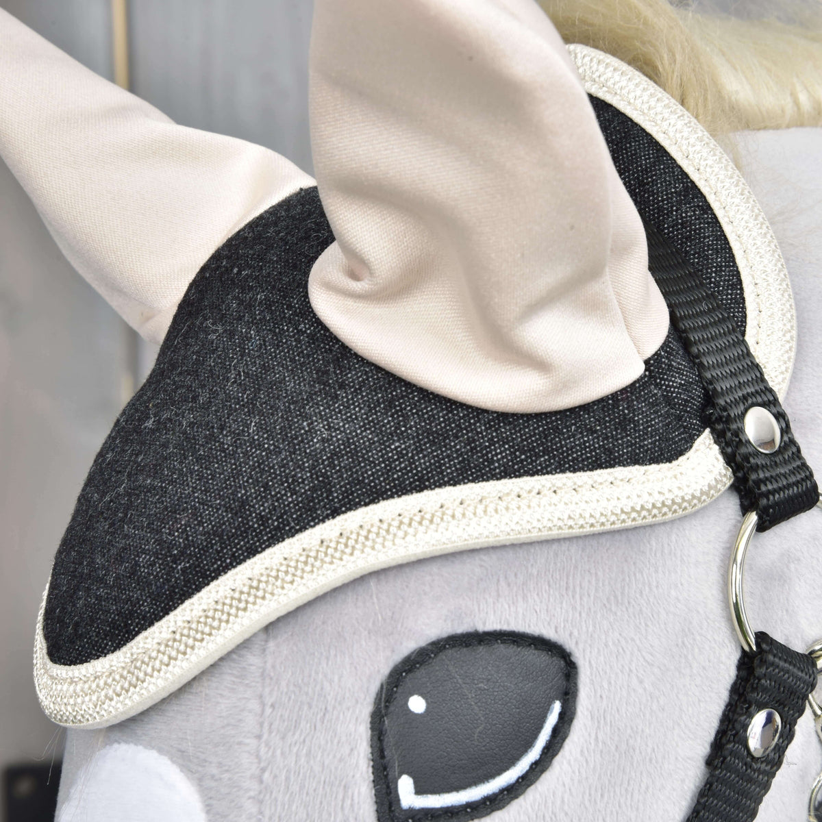 Detail of the denim weave and braided cream edging of the ear bonnet above the eye of a grey plush head