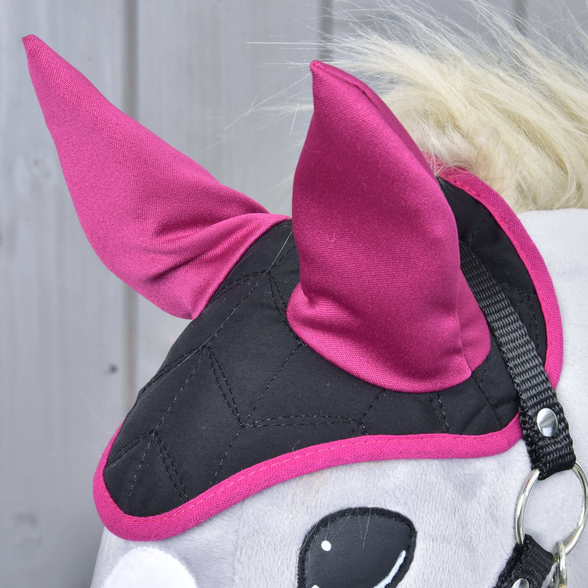 Gros plan sur le bonnet d’oreilles Thermo Ciel : dessus noir matelassé en losanges, oreilles et bordure magenta près d’un licol noir