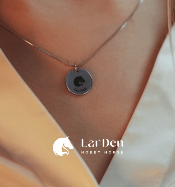 Pendentif rond au logo tête de cheval LarDen porté près du cou sur une chaîne fine, au-dessus d’un col ouvert