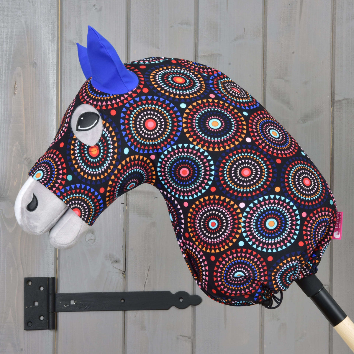 Grijze Hobby Horse van opzij in het beschermpak Alice, kleurrijk mandalapatroon met een trekkoord bij de stok samengetrokken