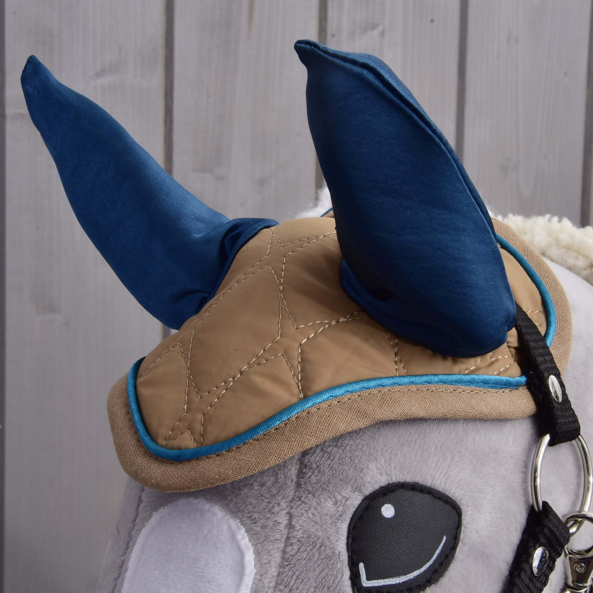 Gros plan sur le bonnet d’oreilles Almond Star aux hautes oreilles marine, matelassage beige en losanges et passepoil bleu sur une tête grise