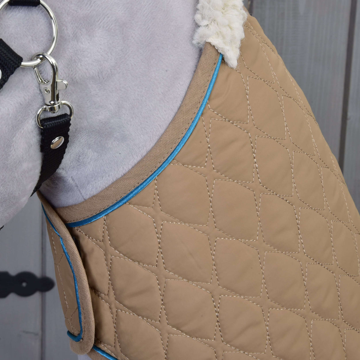 Gros plan sur la couverture beige matelassée en losanges, passepoil bleu et col sherpa crème sur une encolure grise en peluche
