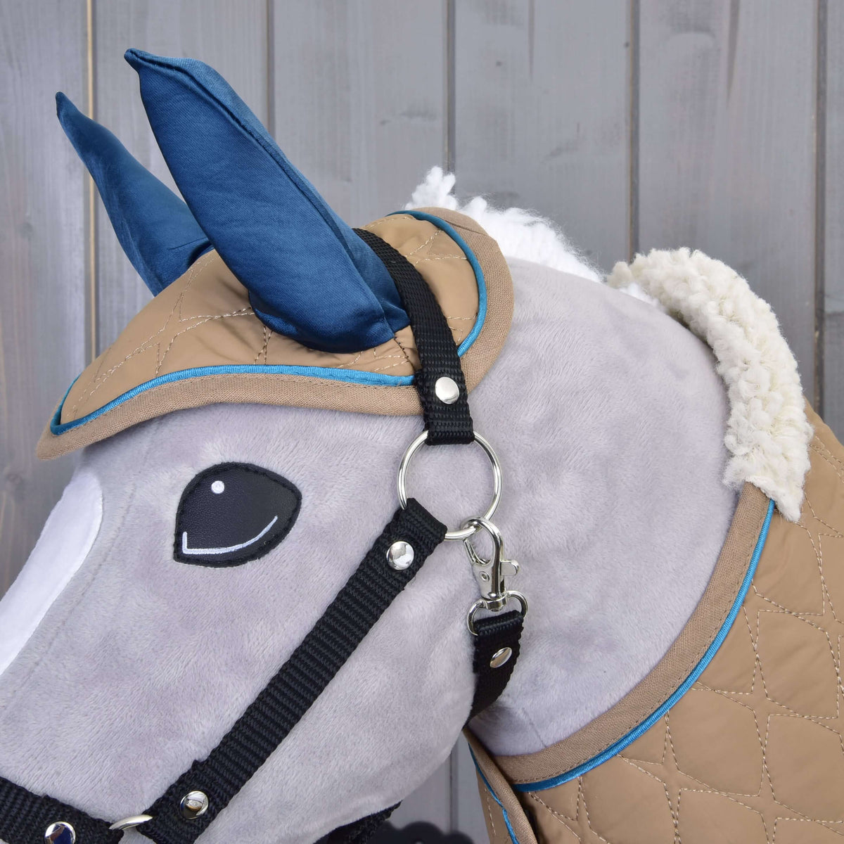 Gros plan sur la tête d’un Hobby Horse gris avec le bonnet d’oreilles Almond Star, licol noir et col sherpa duveteux de la couverture
