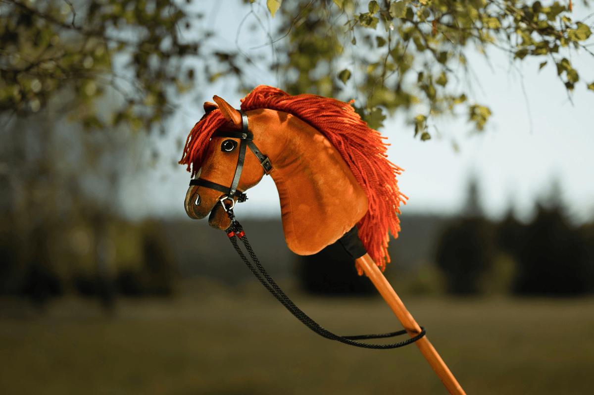 Chestnut Hobby Horse with a red-orange yarn mane and black halter with lead rope under birch leaves