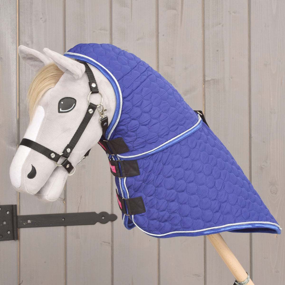 Grijze Hobby Horse in linkerprofiel, van oren tot stok koningsblauw bedekt door de deken Bluebell met halsstuk