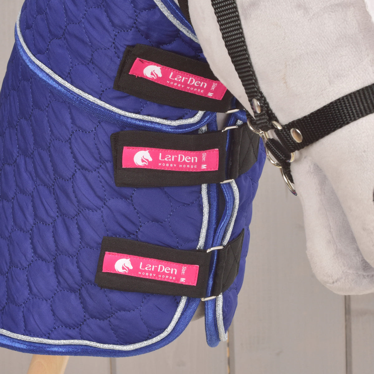 Drie zwarte borstriemen met roze LarDen-labels sluiten de deken met afneembaar halsstuk Bluebell op een grijze Hobby Horse
