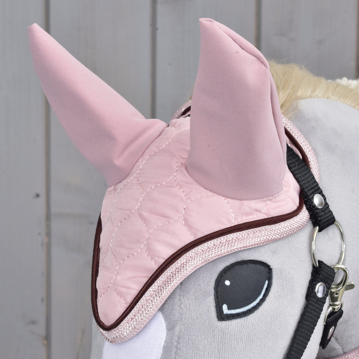 Gros plan sur le bonnet d'oreilles rose matelassé de l'ensemble Blush, oreilles en tissu rose et passepoil marron, sur un Hobby Horse gris