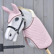 Hobby Horse gris au licol noir portant l'ensemble Blush, couverture matelassée rose et bonnet d'oreilles, devant un mur en bois gris
