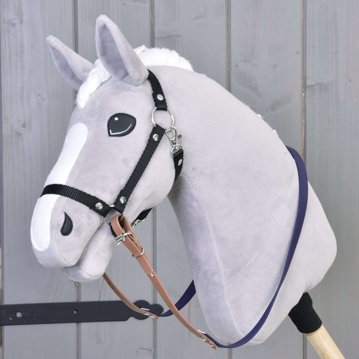 Hobby Horse gris en peluche avec licol noir et rênes caoutchoutées marron et violet foncé le long de l’encolure