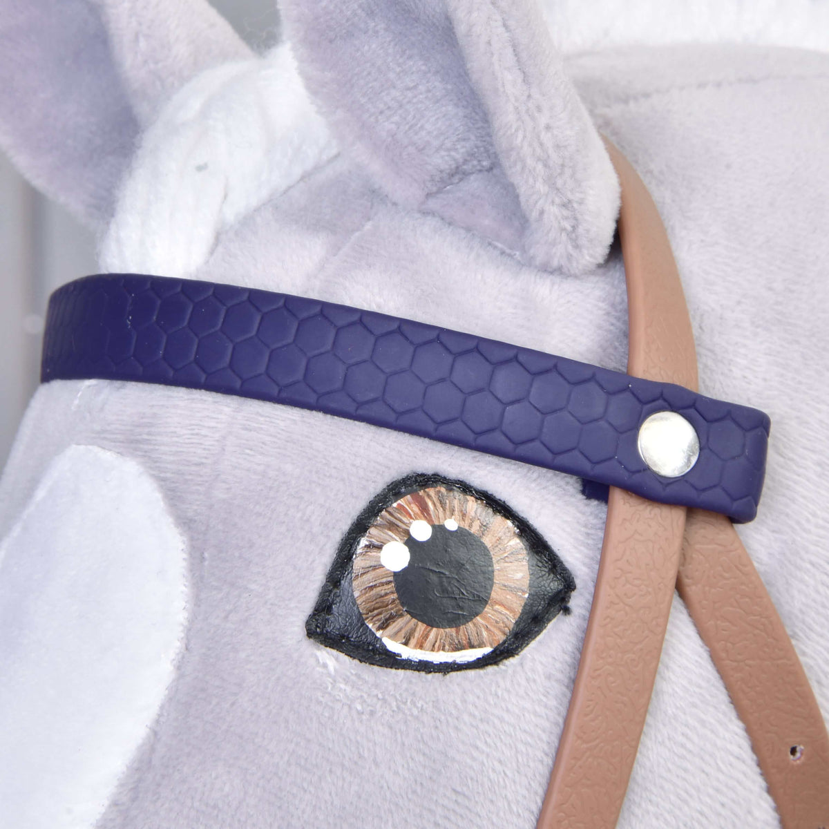 Gros plan sur le frontal violet foncé motif nid d’abeille avec rivet argenté au-dessus de l’œil brun d’un Hobby Horse gris
