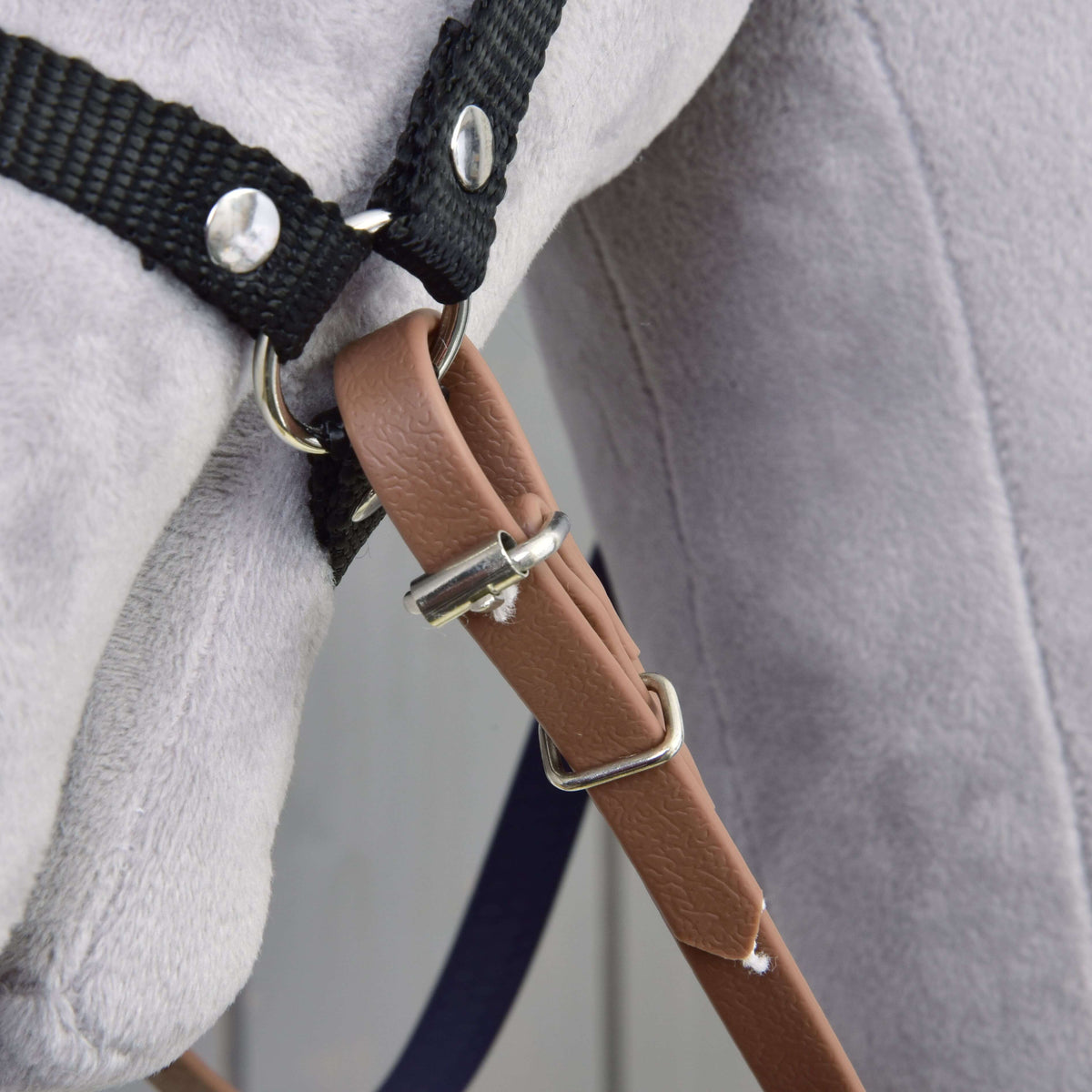 Gros plan sur l’extrémité marron de la rêne, avec boucle et passant, fixée à l’anneau du licol noir d’un Hobby Horse gris