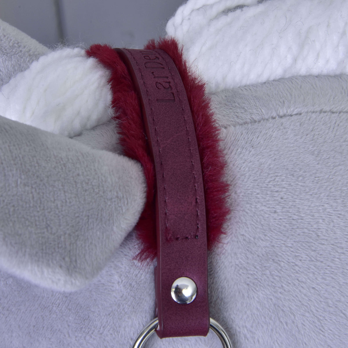 Close-up of the burgundy crownpiece with embossed LarDen logo and fur lining beside the white yarn mane