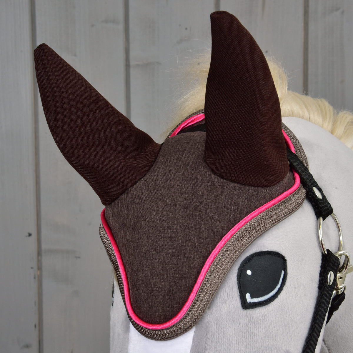 Gros plan sur le bonnet d’oreilles Chocolat sur une tête grise, oreilles marron foncé, devant marron chiné et passepoil rose vif