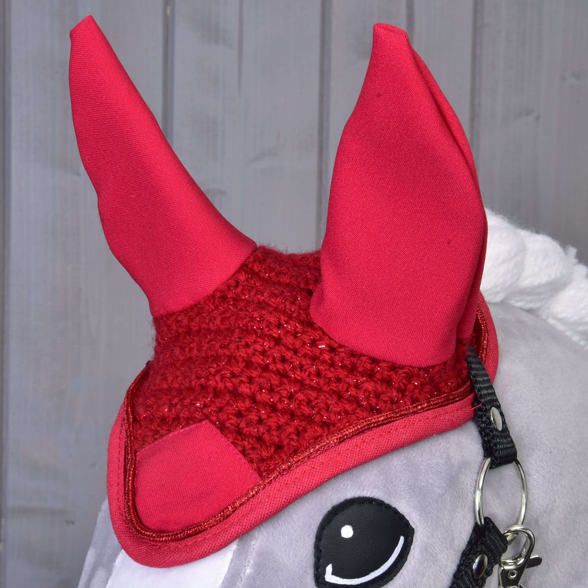 Close-up of the red crocheted ear bonnet with glittering yarn and red binding on a grey Hobby Horse