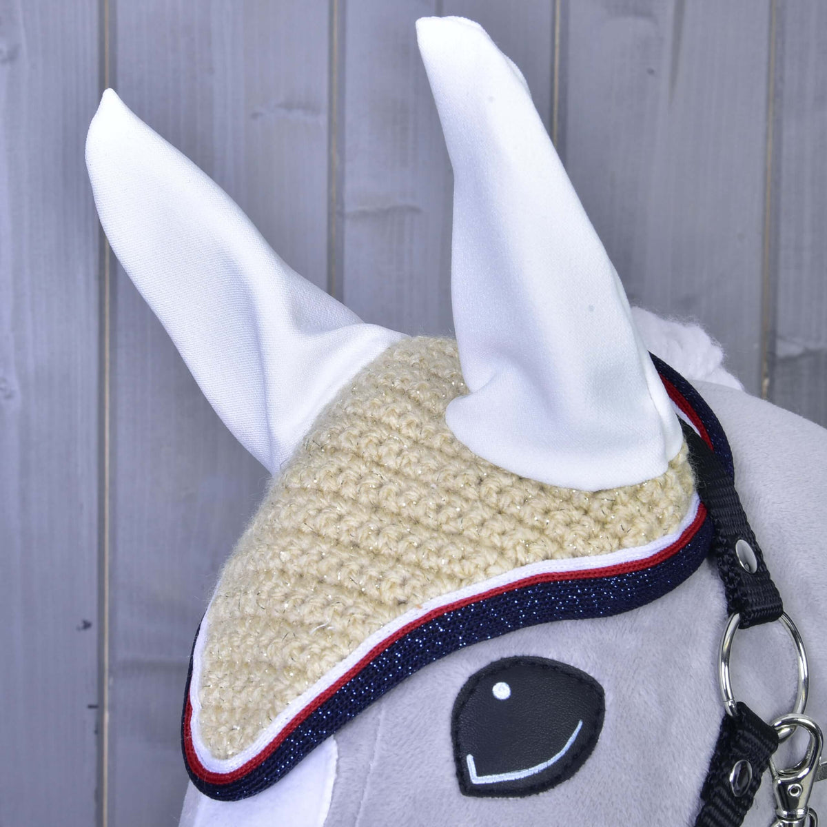 Close-up of the crocheted Nicol ear bonnet: glittery cream stitches, white ear covers and a white, red and navy edging