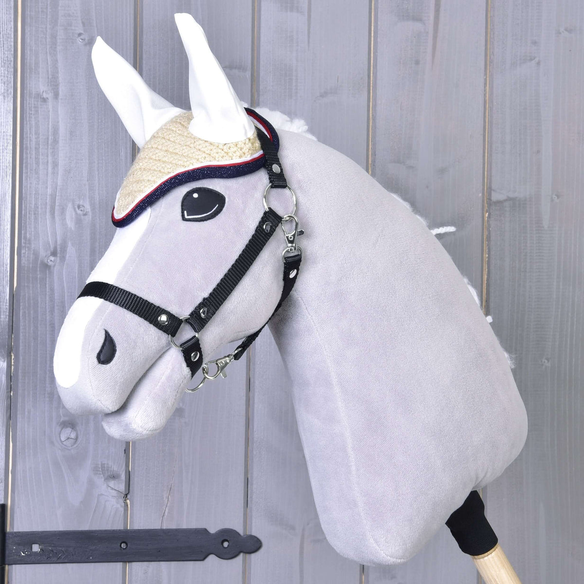 Grey Hobby Horse in a black halter wearing the cream crocheted ear bonnet Nicol with white ears and a red and navy edge