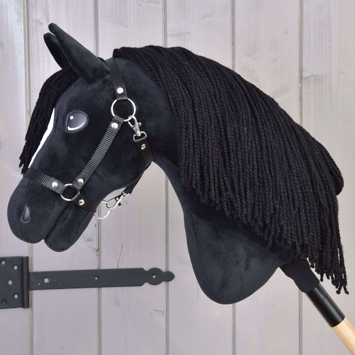 Hobby Horse Cloony in left profile with the long black yarn mane covering the neck, on a wooden stick