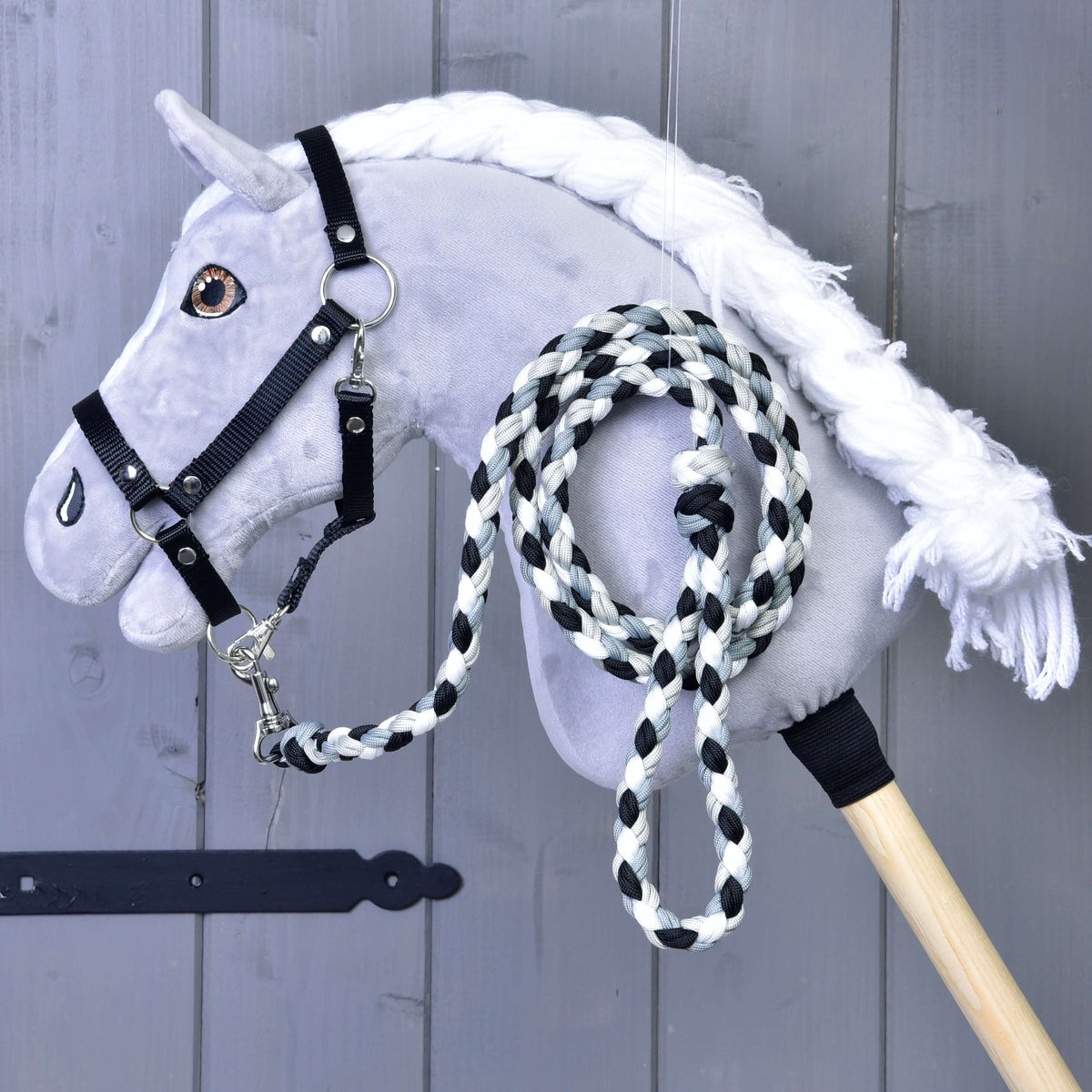A grey plush Hobby Horse in a black halter with the black, white and grey braided lead rope clipped on and coiled