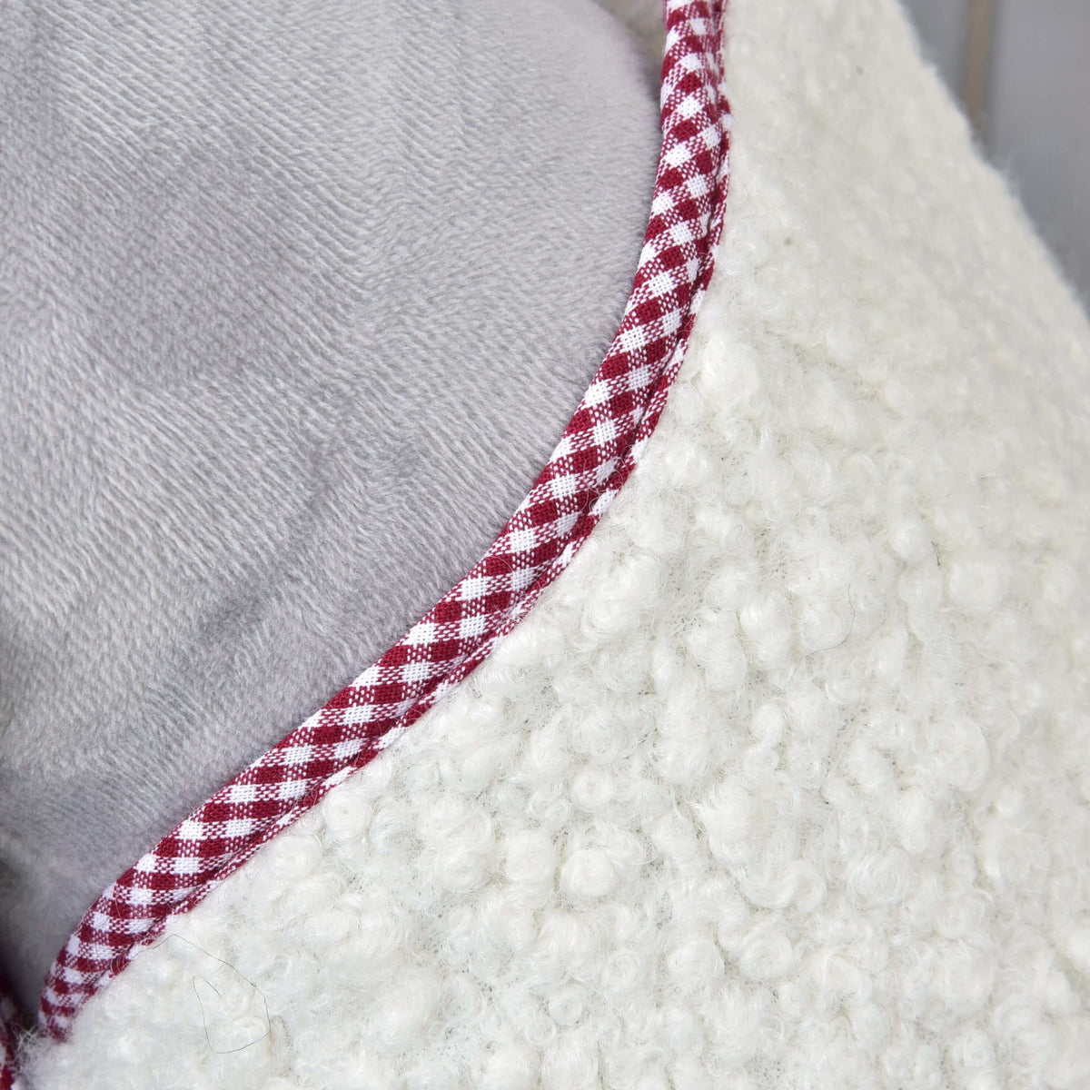 Close-up van de hals van de deken cube rood met rood-wit geruite bies op crème krullend fleece