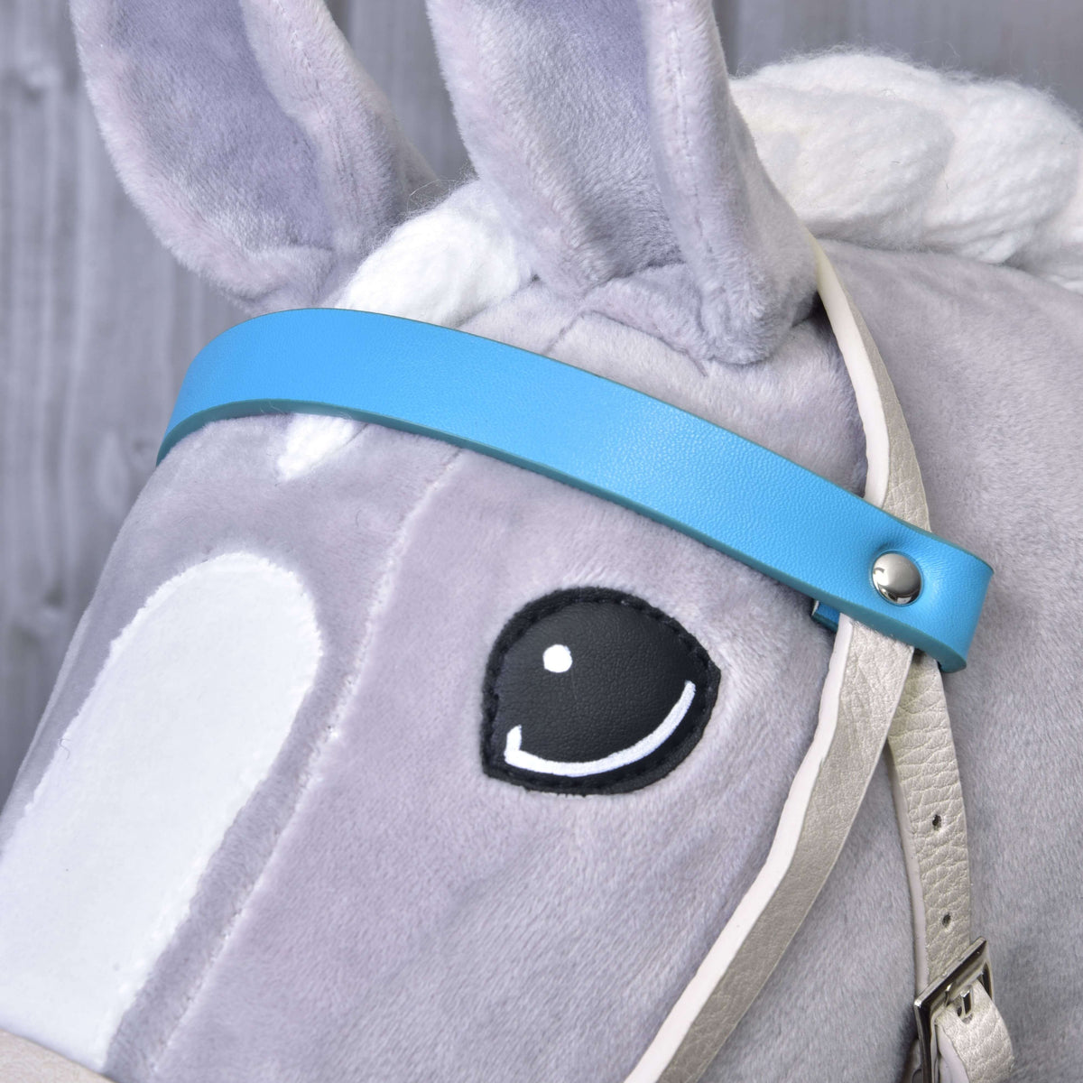 Close-up of the aqua blue leatherette browband with a silver rivet beside the eye of a grey Hobby Horse