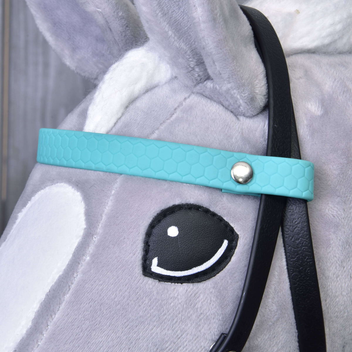 Gros plan sur le frontal turquoise texturé nid d'abeille avec rivet argenté, près de l'œil d'un Hobby Horse gris
