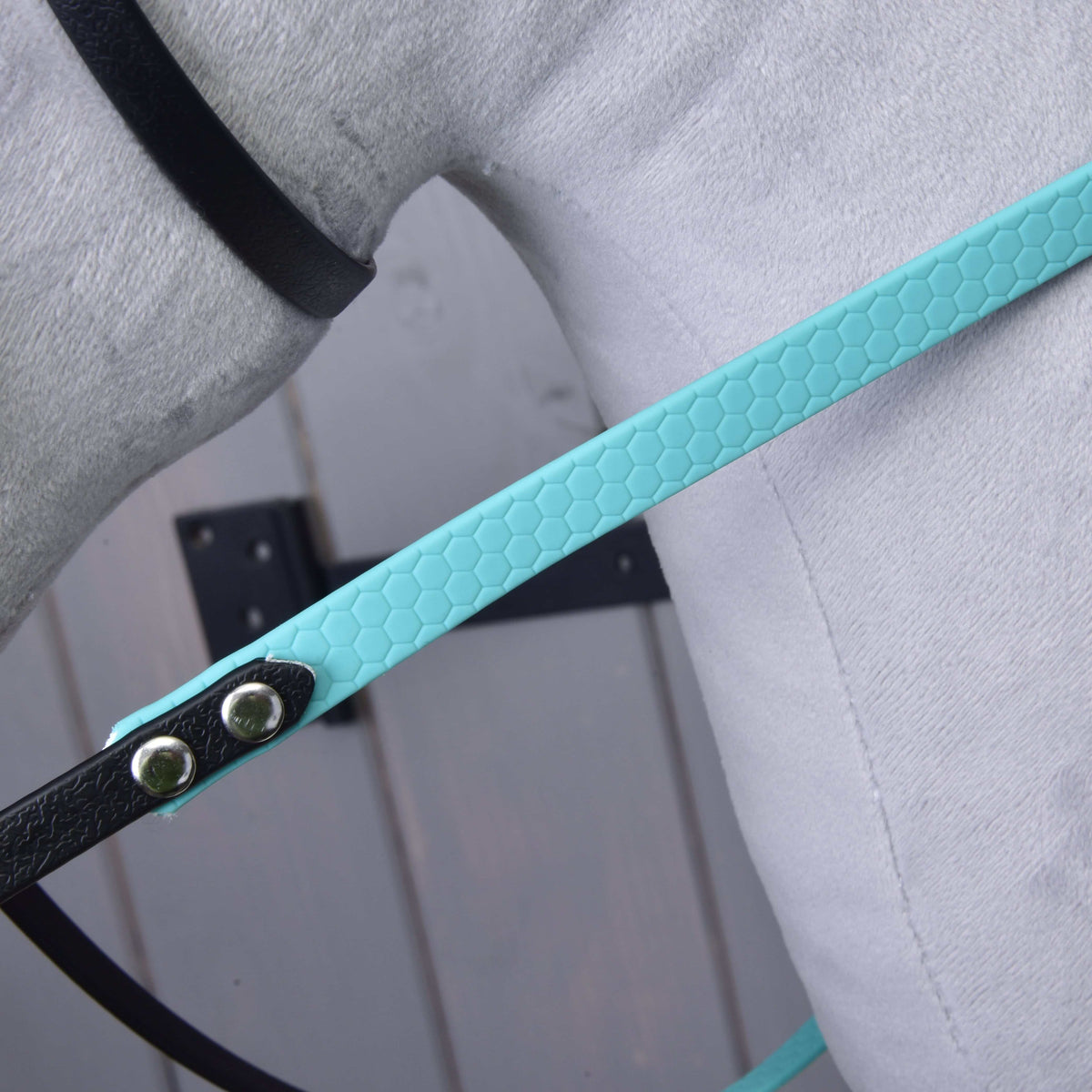 Gros plan sur la rêne turquoise texturée nid d'abeille, rivetée à une courroie noire, sur peluche grise