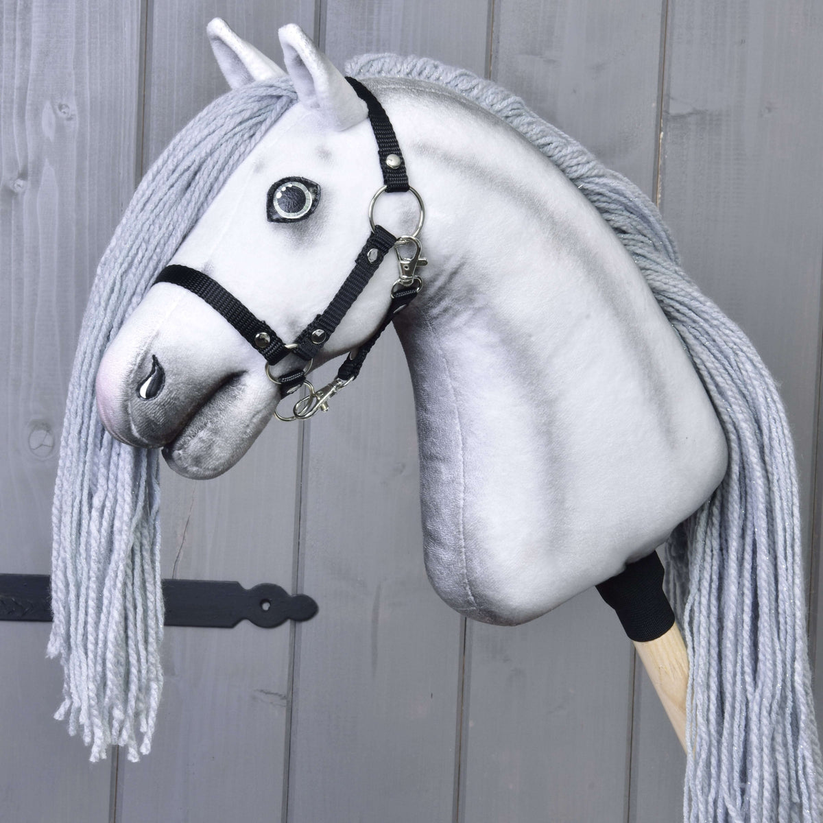 Hobby Horse Licorne Silver présentée sans corne avec licol noir, sur un bâton en bois devant des planches grises