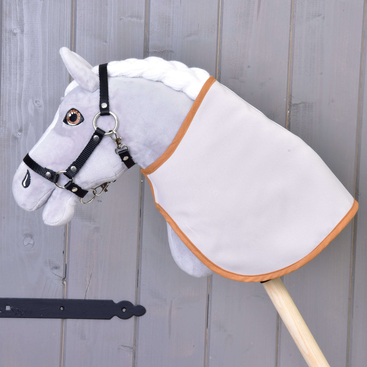 Een grijze pluche Hobby Horse met zwarte halster draagt de deken omgekeerd met de effen lichte kant buiten en karamelkleurige bies